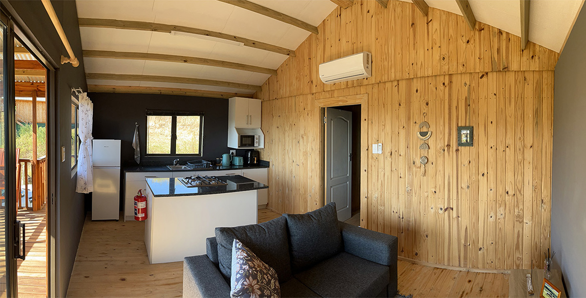 1-Bedroom Riverside Cabin 4: Shalom - Timber-lined interior with lounge and kitchen